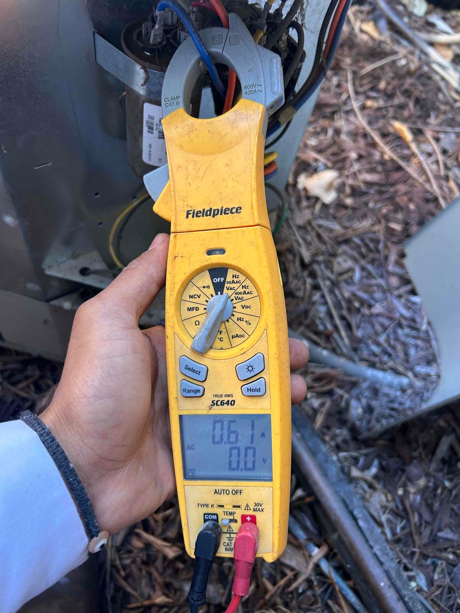 HVAC technician measuring electrical performance at an outdoor air conditioner